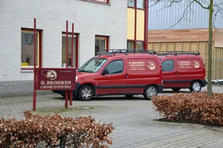 Rode bedrijfsbussen voor het pand, naast het bord G. Broeren Loodgietersbedrijf